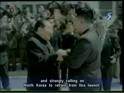 Figure 3. Kim Jong Un still shaking hands with the same person in Figure 2, with the man on the immediate right of Kin Jong Il standing on the right of this photo. Note the door windows in the back and the three stair steps with the rows of people.