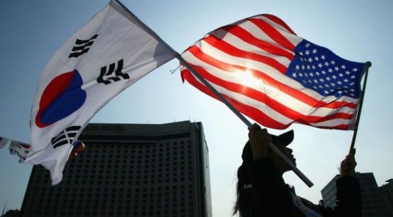 A woman holds to flags of South Korea and the United States against the backdrop of a tall building.